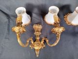 two gold colored wall lights with white shades on a black background