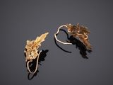 a pair of gold earrings with leaves on them on a black surface