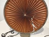 un grand ventilateur marron posé sur une table blanche, muni d'un cordon noir
