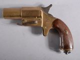 un vieux revolver en laiton avec une crosse en bois, posé sur une surface blanche