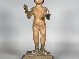 une statue ancienne représentant un garçon tenant une balle, posée sur un socle en bois