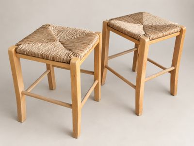 two wooden stools with woven seats against a white background