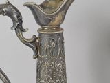 a silver and glass pitcher with a handle on a table