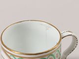 a white cup with a green and gold design on it