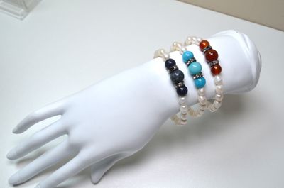 a white mannequin hand holding a bracelet with multi colored beads