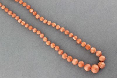 un gros plan sur un collier de perles de corail posé sur une surface grise