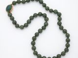 un gros plan d'un collier de perles vertes posé sur une surface blanche