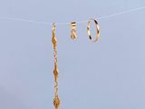 gold earrings hanging from a clothes line with a blue sky in the background
