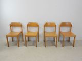 four wooden chairs are lined up against a white wall