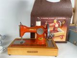 a red sewing machine sitting on a table next to a box