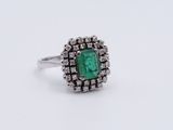 a close up of a ring with an emerald stone surrounded by diamonds