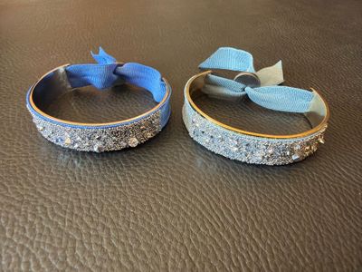 two bracelets with bows on them sitting on a leather surface