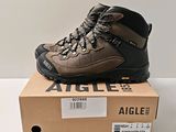 Des chaussures de randonnée pour homme sont posées sur une boîte, sur une surface blanche.