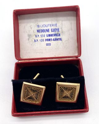 une paire de boutons de manchette dans un coffret rouge posé sur une surface blanche