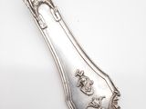 une cuillère ancienne en argent posée sur une surface blanche, ornée d'un oiseau