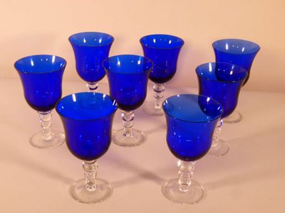 six verres à pied bleus sont alignés sur une surface blanche
