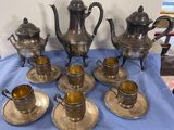 cinq théières en argent et six tasses en argent posées sur une nappe bleue