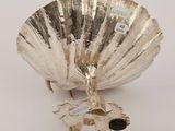 a silver shell shaped object on a white surface with a tag