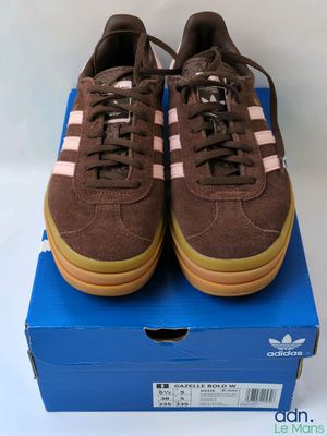 des baskets Adidas marron avec des bandes roses, posées sur une boîte bleue