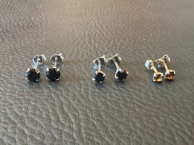 three pairs of stud earrings on a leather surface