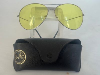 Lunettes de soleil Ray-Ban à verres jaunes, présentées dans un étui sur un fond blanc
