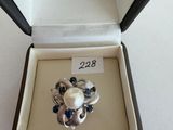 a ring in a box that has a pearl and blue stones in it