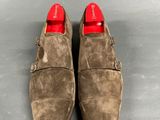 a pair of brown sued shoes with red soles on a gray surface