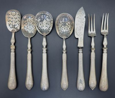 six cuillères et un couteau en métal argenté sont alignés sur un fond gris