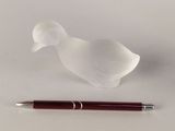 a small glass bird next to a pen on a white surface