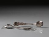 deux cuillères en argent et un repose-cuillère posés sur une surface blanche