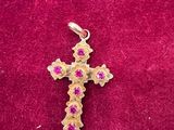 une croix en or sertie de pierres roses, posée sur un fond de velours rouge