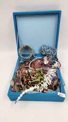 une boîte bleue remplie de bijoux variés, posée sur une surface blanche