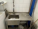 a sink in the corner of a kitchen with a trash can