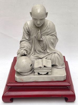 statue d'un moine assis sur un socle rouge, tenant un livre et une balle