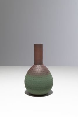 un vase vert et marron posé sur une surface blanche