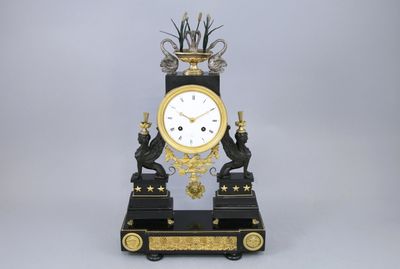 une horloge noire et dorée surmontée d'un oiseau