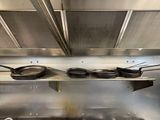 several pans are lined up on a metal shelf in a kitchen
