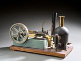 une petite maquette de machine à vapeur posée sur un socle en bois