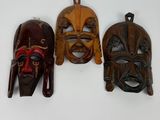 trois masques en bois accrochés à un mur sur un fond blanc