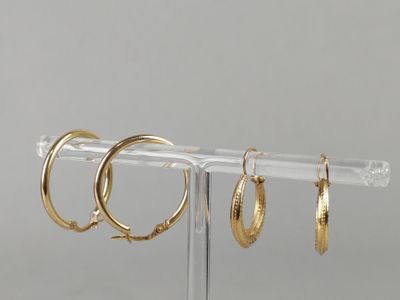 three pairs of gold hoop earrings on a clear display stand