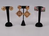 three pairs of earrings on a black stand