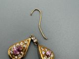 paire de boucles d'oreilles ornées de pierres roses et blanches sur un fond gris