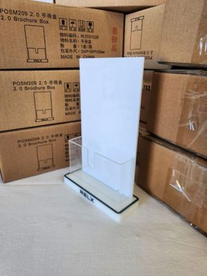 a white sign on a clear stand in front of a stack of boxes