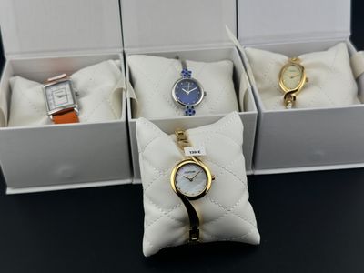 trois montres se trouvent dans une boîte posée sur une table, avec un coussin à côté