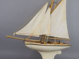 an old model of a sailboat with white sails on a wooden stand