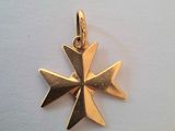 un gros plan d'un pendentif en forme de croix en or posé sur une surface blanche
