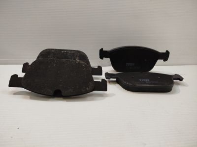 deux plaquettes de frein noires posées sur une surface blanche, sur fond blanc