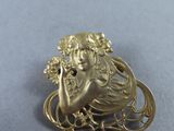 an image of a gold broochle with a woman holding flowers