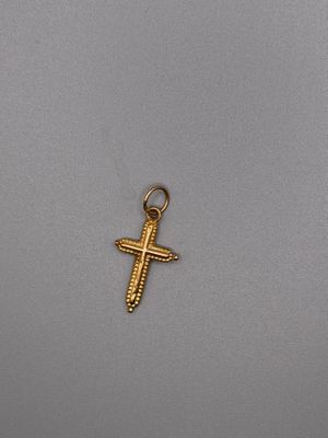 un petit pendentif en forme de croix en or sur un fond gris