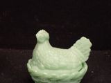 a green ceramic chicken sitting on top of a black surface
